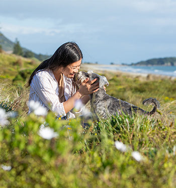Woman smiling giving her miniature schnauzer nose kisses infront of Mount Maunganui