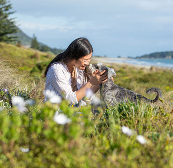 Young woman smiling giving her miniature schnauzer nose kisses infront of Mount Maunganui